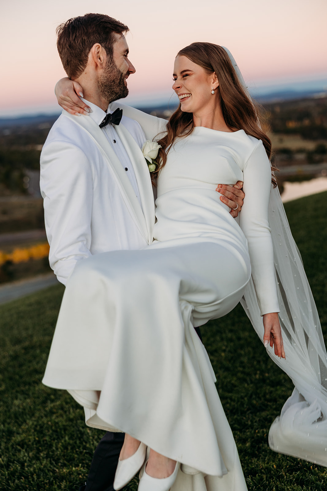 Bride scooped up and spun around by her groom. Looking at each other and smiling. Taken during sunset at the National Arboretum Canberra by Acacia & Grace Photography