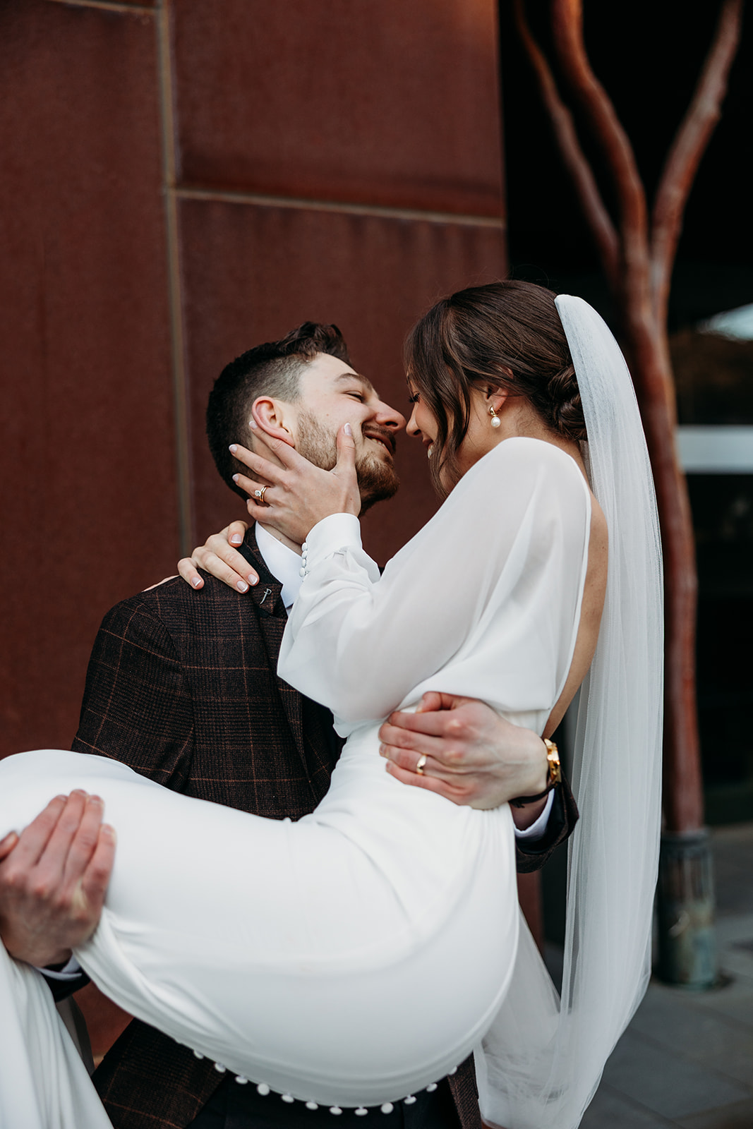 Groom carries bride as they smile and share a kiss. Photo taken at New Acton Canberra by Wedding Photographer Acacia & Grace